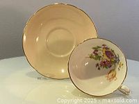 Photo of the cream colored saucer with scalloped edges and gold trim.