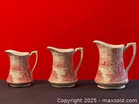 Front view of three ceramic pitchers varying in height against a red background