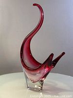 Front-left angled view of the vintage red cranberry hand blown glass sculpture showing its sweeping upward tail and clear glass base.