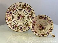 Cup and saucer set showing bramble fruit pattern and gold accents from front angle.