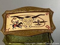 Full top view of the brass cowboy belt buckle showing the embossed border and hand painted western scene central design.