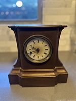 Front view of the antique mantle clock, showing the clock face with Roman numerals and the wooden case with detailed edges.