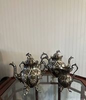 Photo showing side angle of all three pieces: coffee pot, tea pot, and creamer, highlighting detailed engravings and handles.