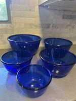 Five cobalt blue glass mixing bowls nested and arranged on a kitchen counter, showing the size range and color.