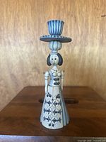 Front view of porcelain figurine candle holder depicting a woman with floral decorations on dress and detailed head with candle holder on top.