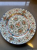Top view of the porcelain plate showing the floral Imari Blossoms pattern with red flowers, green leaves, and gold accents on white.