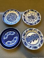Top view of all four plates showing different intricate cobalt blue hand-painted Japanese designs on white porcelain.