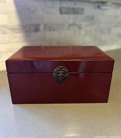 Front view of red lacquered wooden case on countertop, showing rectangular shape and glossy finish.
