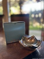 Star-shaped mini bowl made of Nambe Alloy next to its original box, showing smooth reflective surface and five raised curved points.