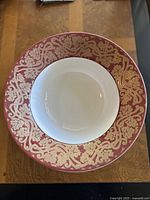 Top view of a white porcelain bowl with a wide burgundy and gold scroll pattern border.