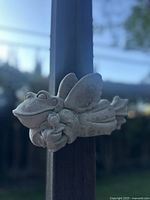 Close-up of the frog angel wall art piece mounted on a wooden post, showing the frog's face and tulip flowers.