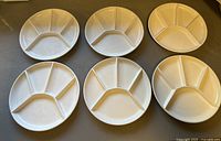 Set of six ivory ceramic divided fondue plates arranged on a surface, showing consistent design and size.