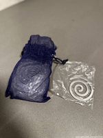 Set of silver spiral napkin rings inside blue organza pouch, one ring visible, placed on neutral surface.