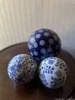 Three porcelain floral orbs on brown table against striped wall