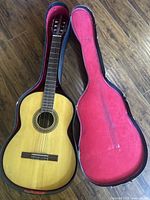 Full view of vintage acoustic guitar inside hard case with red velvet lining