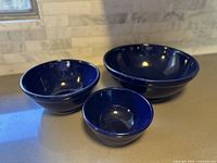 Three cobalt blue handmade pottery bowls displayed side by side showing front and side profiles, illustrating size difference and nesting capability.