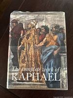 Photo of the book's front cover dust jacket featuring Renaissance artwork and the title 'The Complete Work of Raphael'. Cover shows some wear and wrinkling.