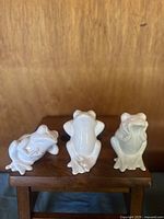 Front and top view of the three porcelain frog figurines in the "Three Wise Monkeys" pose on a wooden surface.