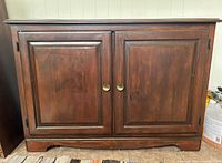 Front view of the wooden cupboard showing double paneled doors with brass round knobs.