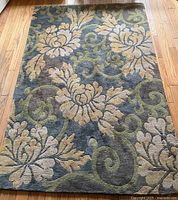 Top view of hand knotted wool rug with floral pattern in green, beige, and grey-blue.