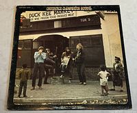 Front cover photo of the vinyl album showing band members outside a store, album title and artist name visible.