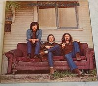 Front cover of the vinyl album showing the three band members seated on a couch outdoors.
