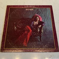 Front cover of the vintage vinyl album 'Pearl' showing Janis Joplin seated on an ornate chair with a dark textured background and the word 'Pearl' above her.