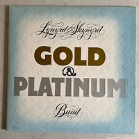 Front cover of the Lynyrd Skynyrd Gold & Platinum vinyl album showing embossed gold and silver lettering on light blue to white gradient background.