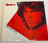 Front cover of the vinyl album featuring a close-up image of a band member in red and black with 'The Doors' logo and 'Greatest Hits' text.