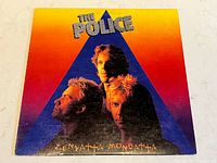 Front cover of The Police's Zenyatta Mondatta vinyl album showing band members within blue triangle over gradient background