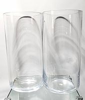Two large clear cylindrical glass vases side by side on white surface