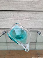 Clear and turquoise freeform leaf-shaped art glass dish shown from top and side angles on glass surface.