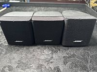 Front view of three black Bose satellite speakers aligned side by side showing fabric grills and Bose logos