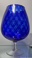 Blue wine glass with broad rounded bowl and clear stem/base photographed against neutral background.