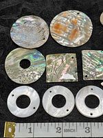 Top close view of various large and small abalone and mother of pearl shell pieces showing iridescence and drilled holes for jewelry crafting.