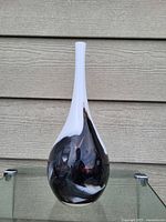 Front view of Murano style teardrop vase showing white elongated neck and swirled black and white body on glass surface