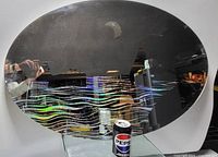 Oval mirror with moon and wave designs placed on a glass stand with a Pepsi can for scale.