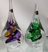 Front angle of both glass paper weights together showing swirling interior designs in purple, orange, and green colors.