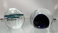 View of two glass abstract paper weights, showing a blue and green leaf-like design inside one and a dark blue core inside the other.