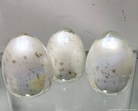 Three translucent, iridescent glass egg-shaped paperweights with amber flecks, all in excellent condition.