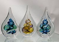 Front view of all three tear drop-shaped glass paperweights with colored swirls inside on a white background.