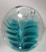 Front view of small glass paper weight showing blue-green layered abstract design with air bubbles inside.