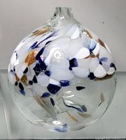 Front view of a clear glass orb with embedded white, blue, and gold colored accents. The neck is narrow and the orb is round shaped.