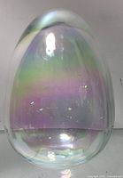 Front view of the small rounded egg-shaped glass ornament showing iridescent multi colored hues.