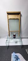 Full view of vintage wooden washboard with glass scrubbing panel standing vertically against white background. A soda can at base provides scale reference.