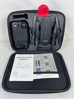 Carrying case open showing the drone, remote controller, instruction manual, extra propellers, and charging cable securely placed in foam compartments.