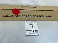 Closed cardboard box labeled 'XIMI-V OFFICE LED SCREEN LIGHT' with a user manual placed on top, showing product packaging and documentation.