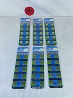 Full view of all six unopened cards of T&E alkaline button cell batteries laid flat in two rows of three on white surface with label #42 visible.