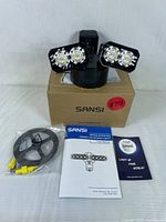 Sansi security LED light on top of its branded box, includes mounting cable and instruction manual.
