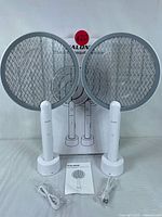 Set of two PALONE electric mosquito swatters standing on their charging docks with original packaging behind.